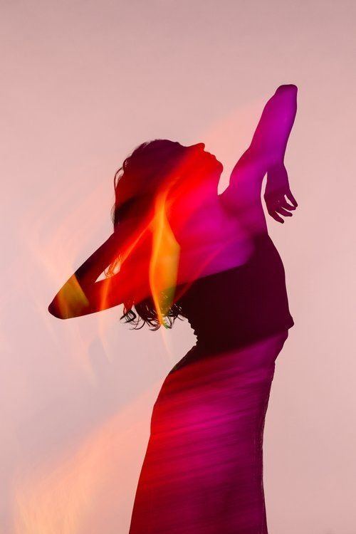 A dancer silhouetted in washes of magenta, coral, and gold light, head thrown back, one arm reaching upward